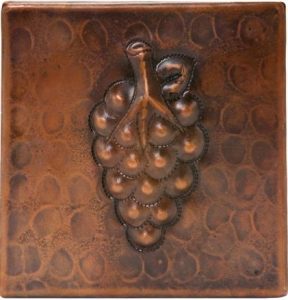 A metal tile with a copper raised grape.