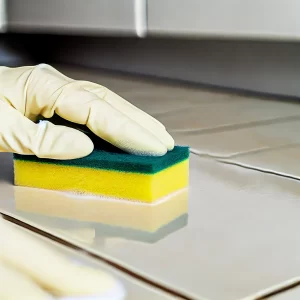 A person cleaning tile surfaces with a sponge and tile cleaner.